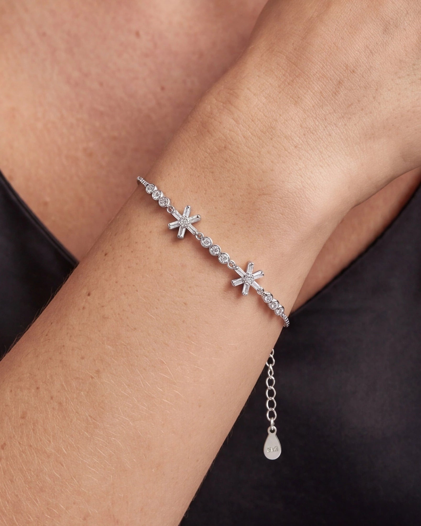 Silver bracelet with star-shaped charms on a wrist against a dark background #color_silver