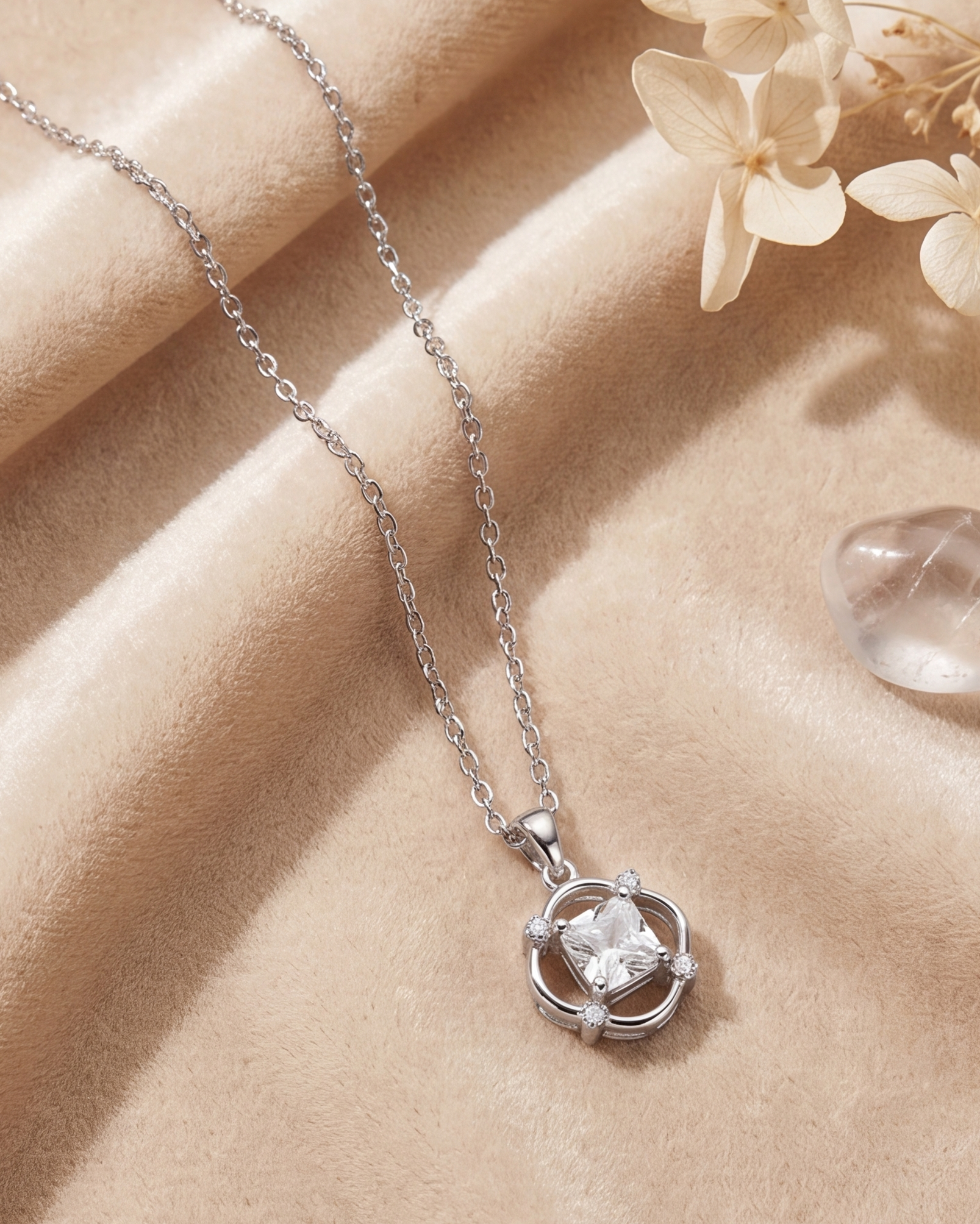 Silver necklace with a pendant on a beige surface with flowers and a crystal. #color_silver