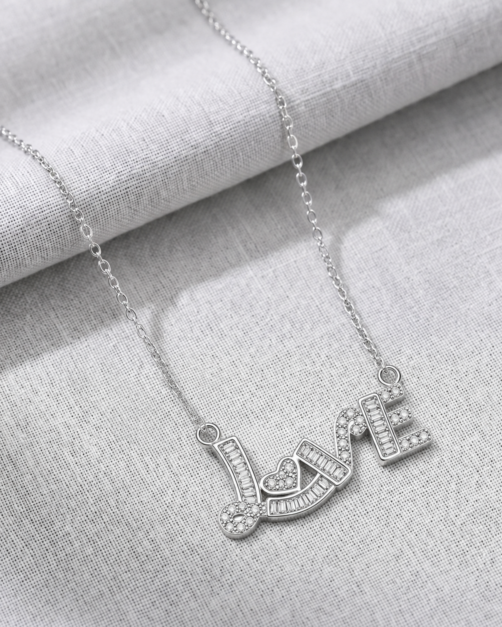 Silver 'LOVE' necklace on a light gray fabric background #color_silver