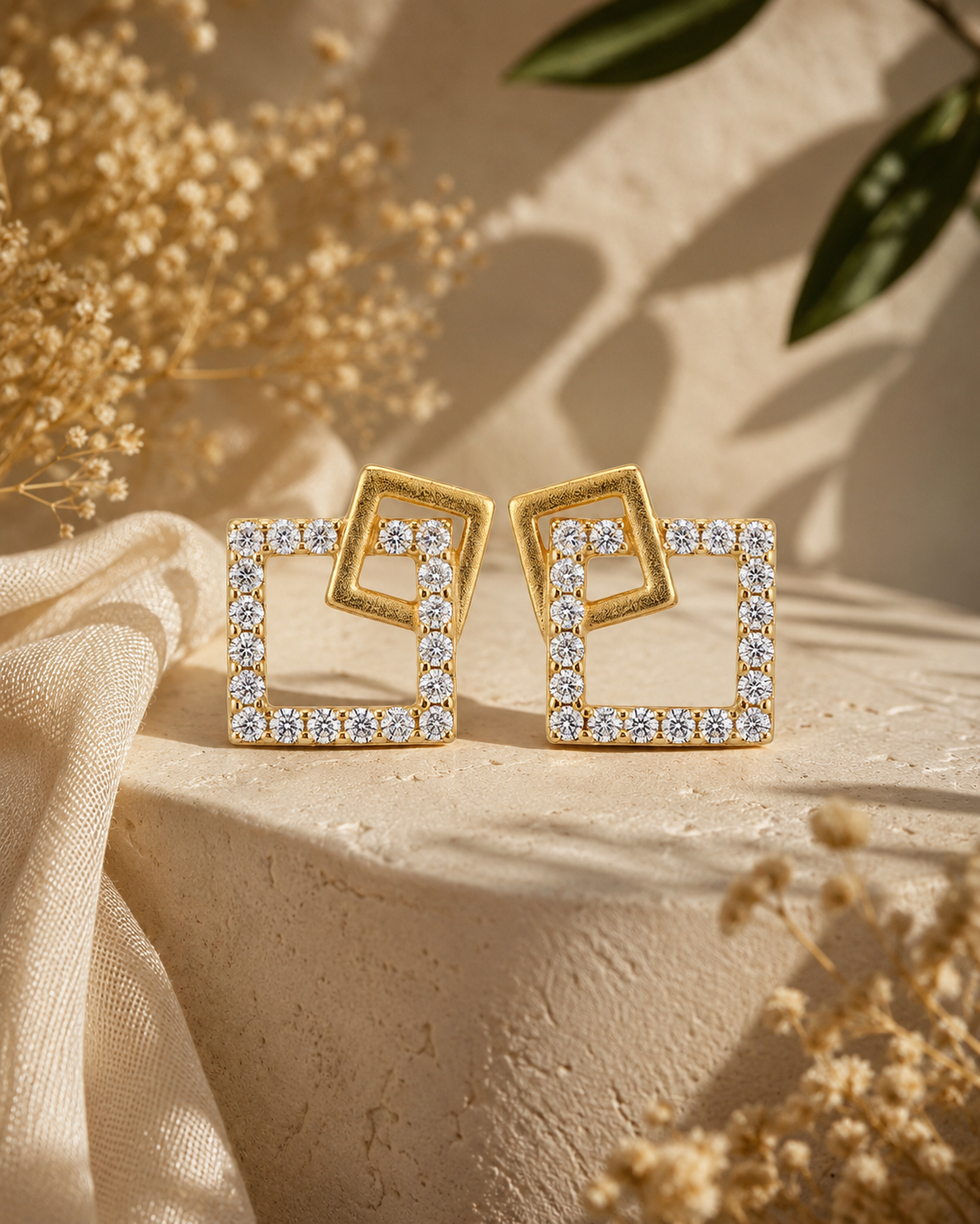 Gold square earrings with clear stones on a beige surface with dried flowers and leaves #color_gold