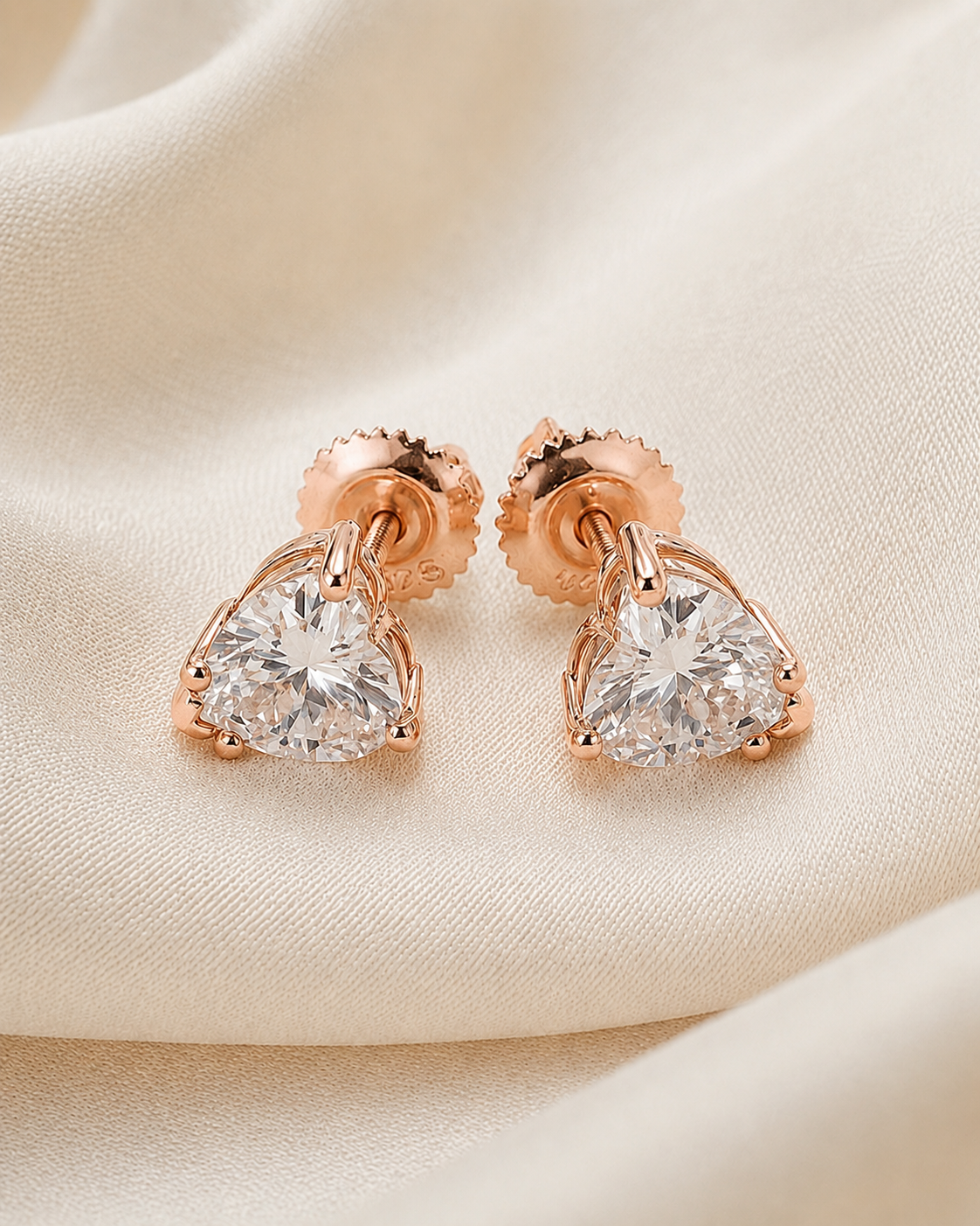 Rose gold heart-shaped diamond earrings on a soft beige background