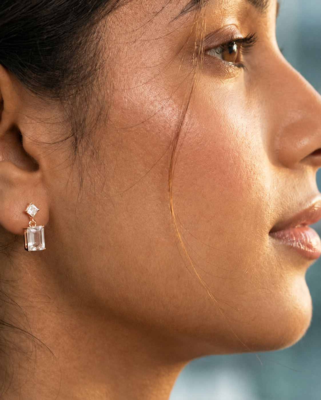 Close-up of a woman's face wearing diamond earrings with a blurred background #color_rose gold