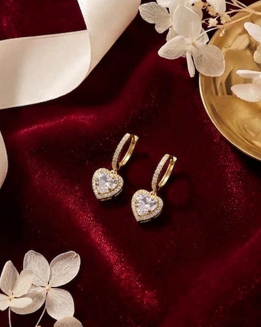 Heart-shaped earrings on a red velvet surface with white flowers#color_gold