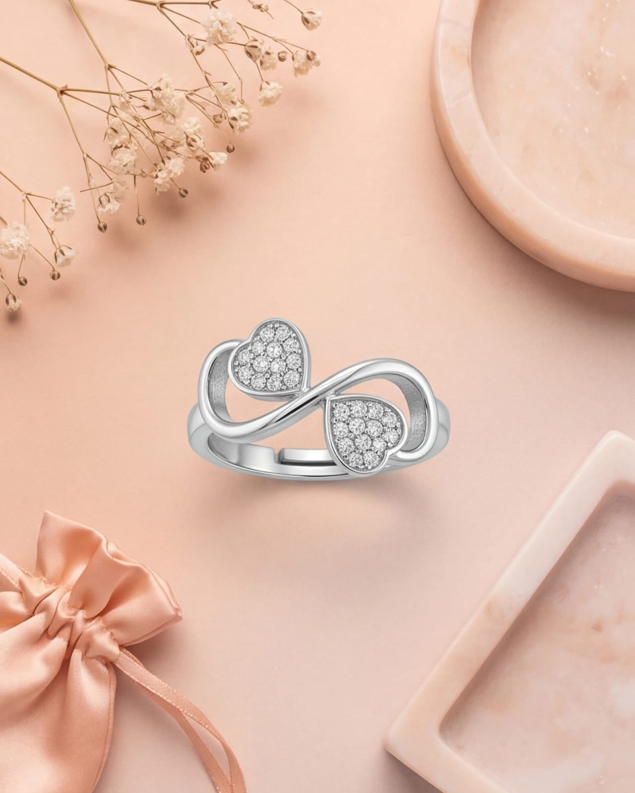 Silver ring with heart-shaped gemstones on a pink surface with decorative elements # color_silver
