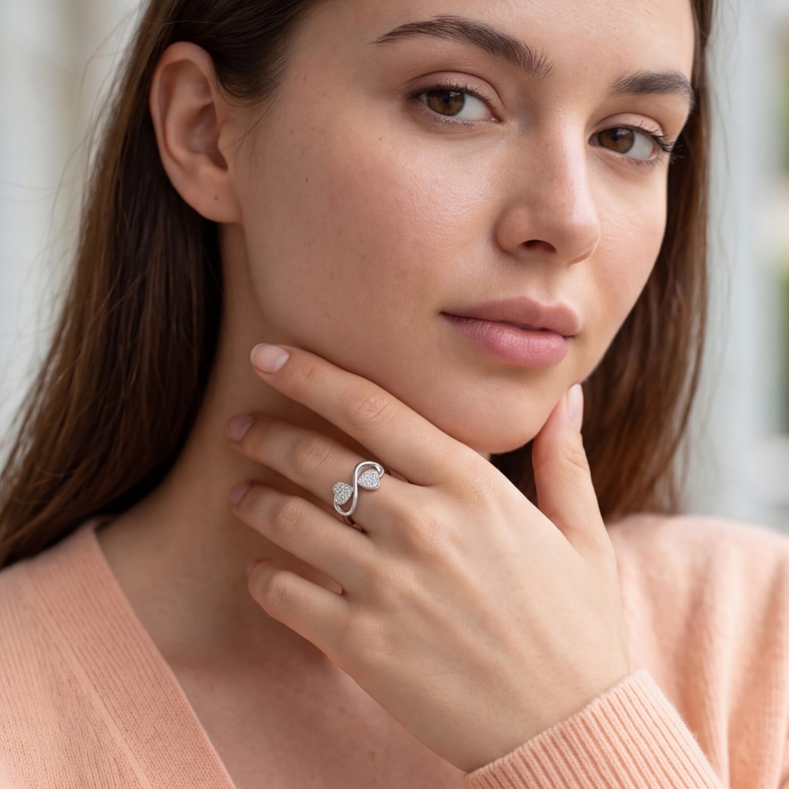 Woman wearing a ring with an infinity symbol, close-up of face and hand. #color_silver