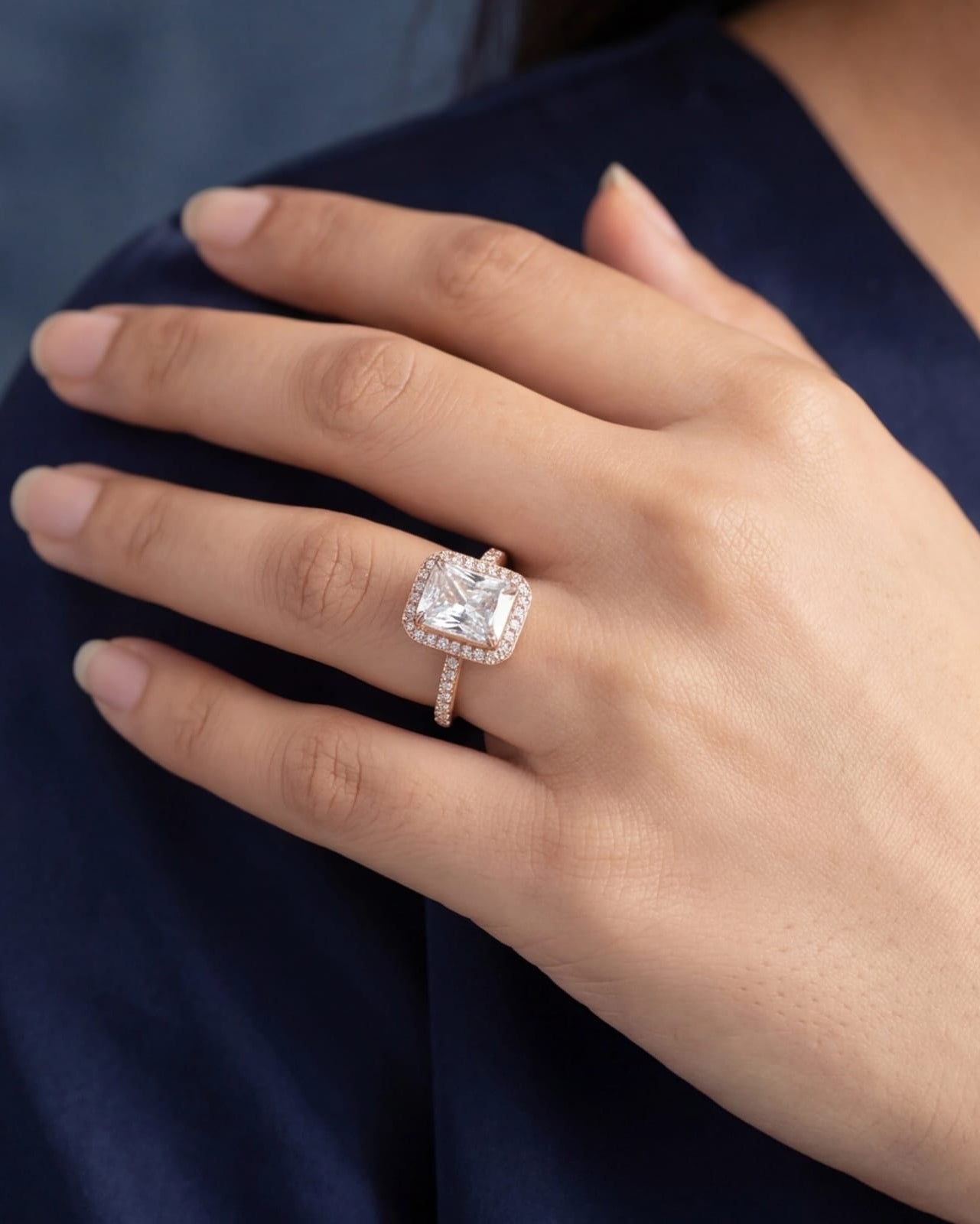 Hand wearing a diamond ring with a dark blue fabric background #color_rose gold