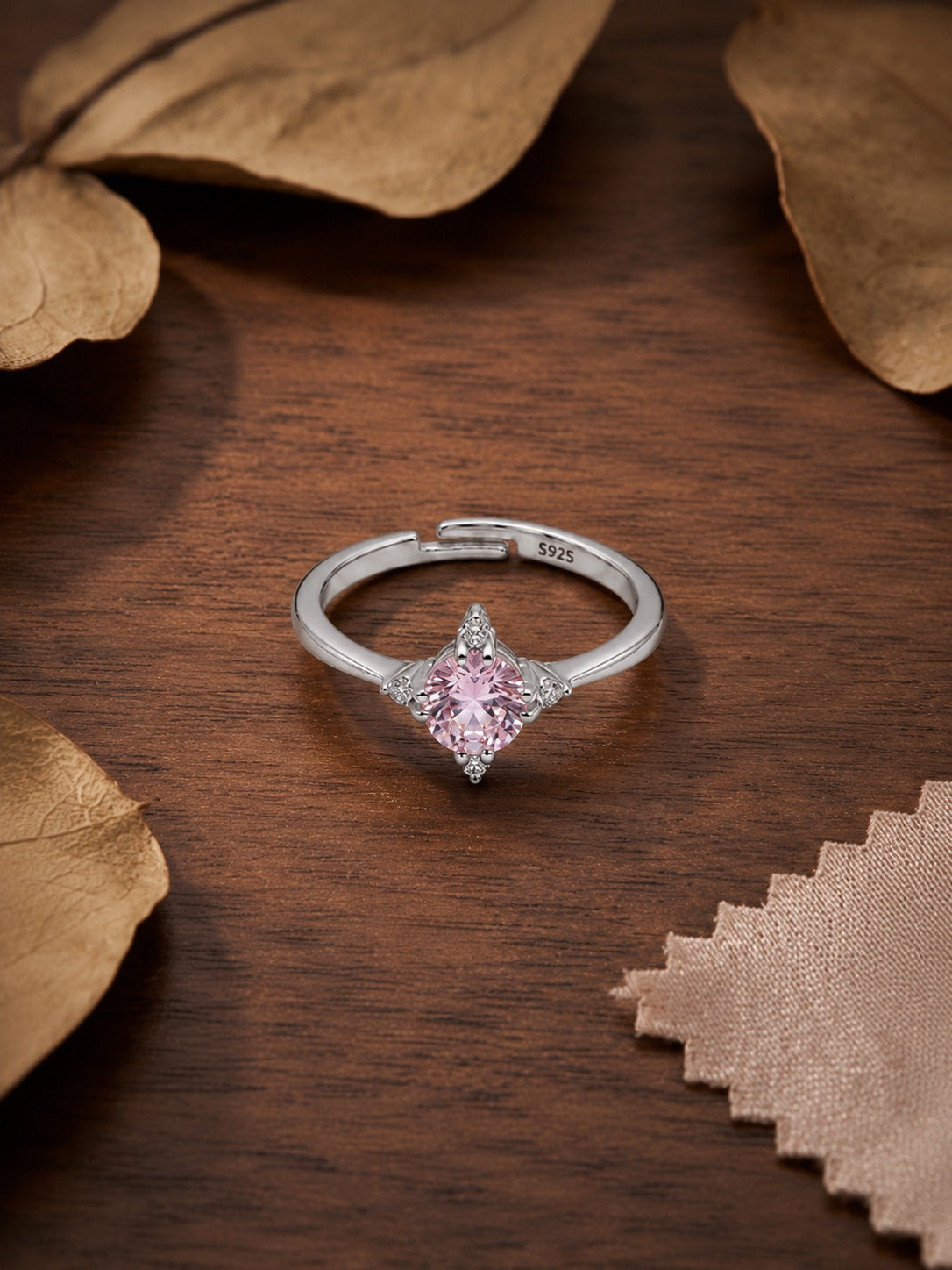Silver ring with a pink gemstone on a wooden surface with leaves #color_silver