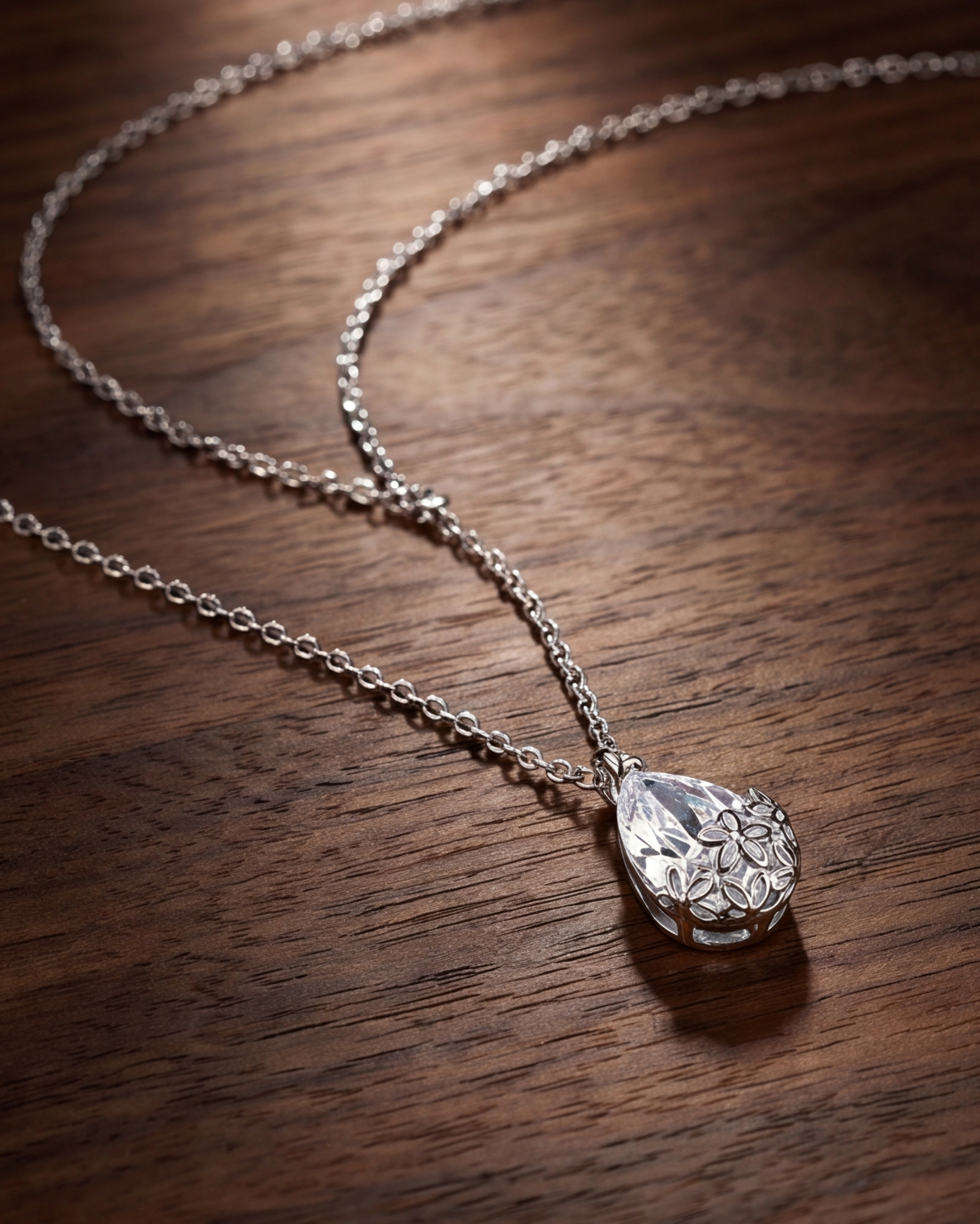 Silver necklace with a teardrop-shaped pendant on a wooden surface #color_silver