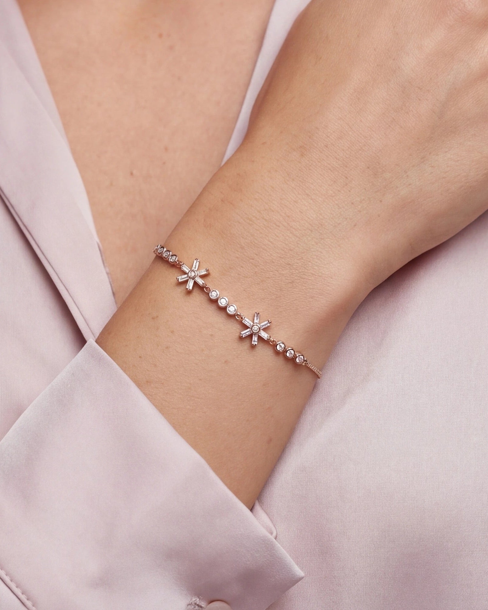 Bracelet with star-shaped charms on a wrist against a light pink  background #color_rose gold
