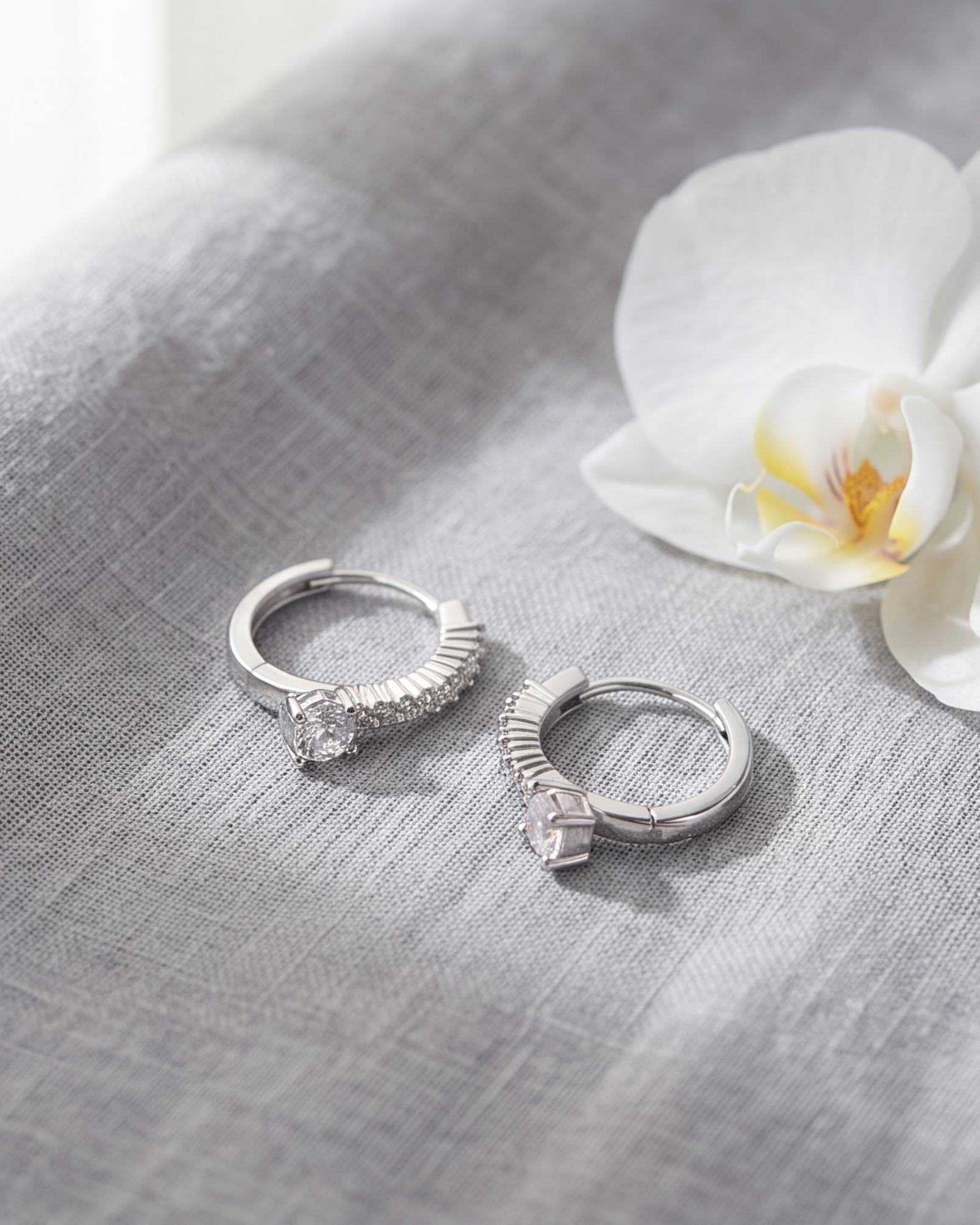 Two silver rings on a gray fabric surface with a white flower.