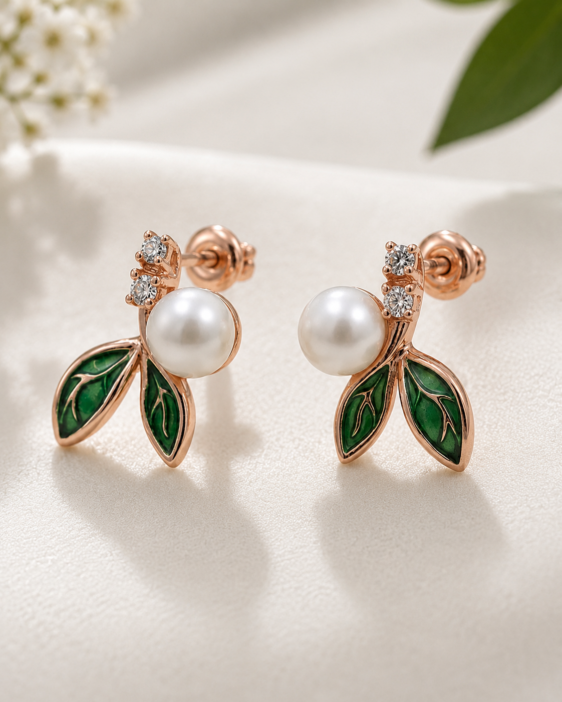 Pair of earrings with pearl-like centers, green leaves, and rose gold accents on a light background  #color_rose gold 