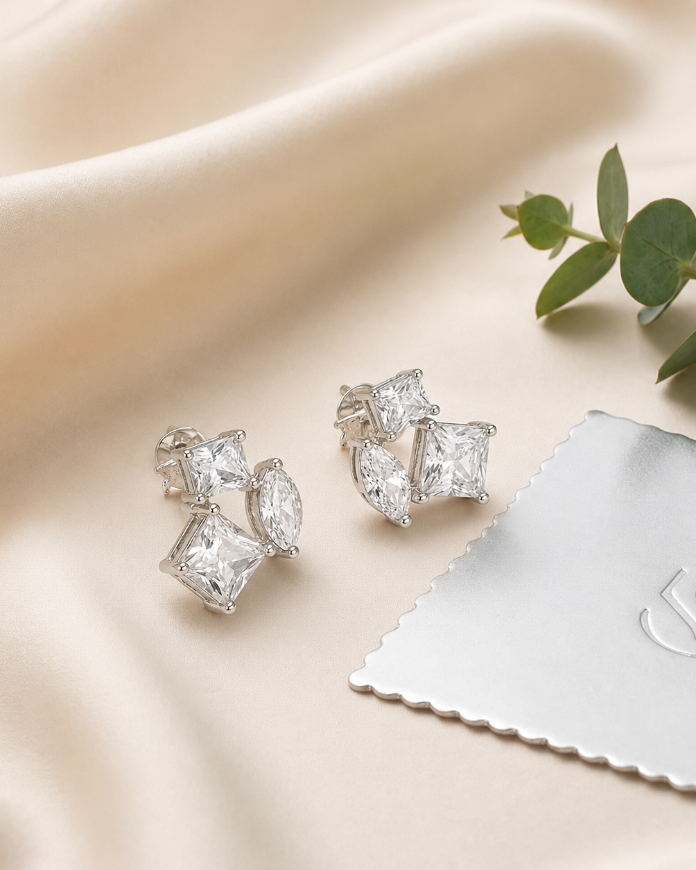 Pair of silver earrings with clear gemstones on a beige fabric background with a branded cloth #color_silver