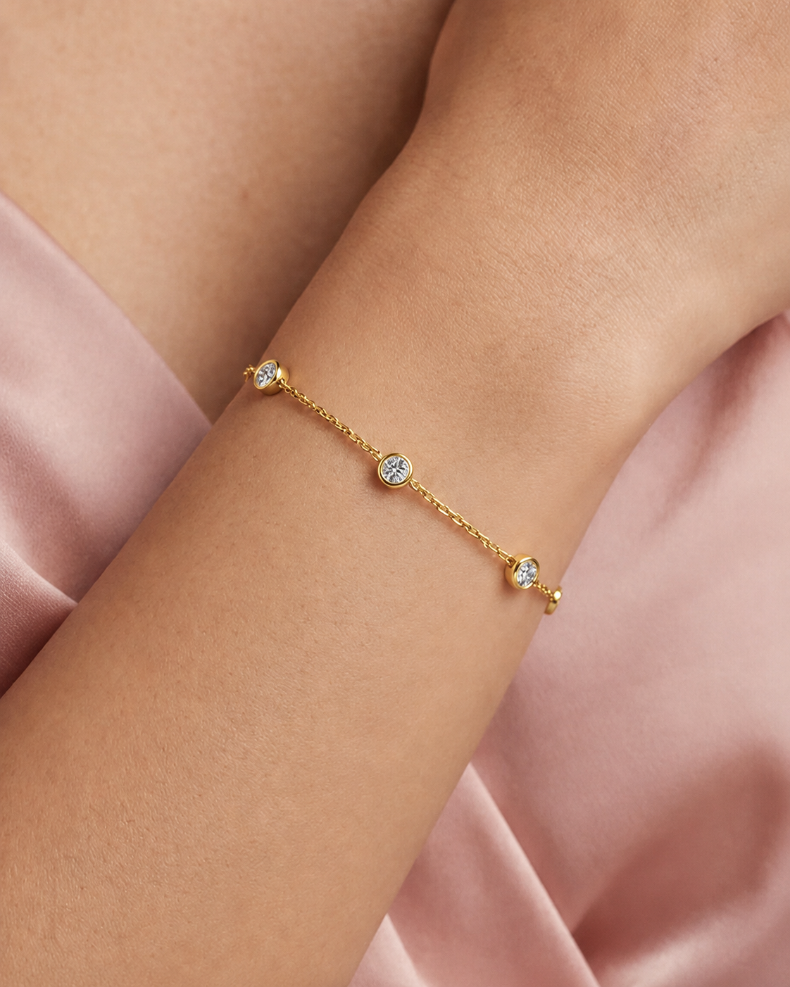 Gold bracelet with gemstones on a wrist against a pink fabric background #colour gold
