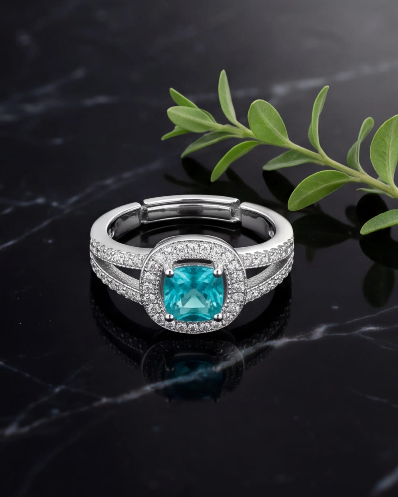 Silver ring with a blue gemstone on a dark surface with a green leaf.