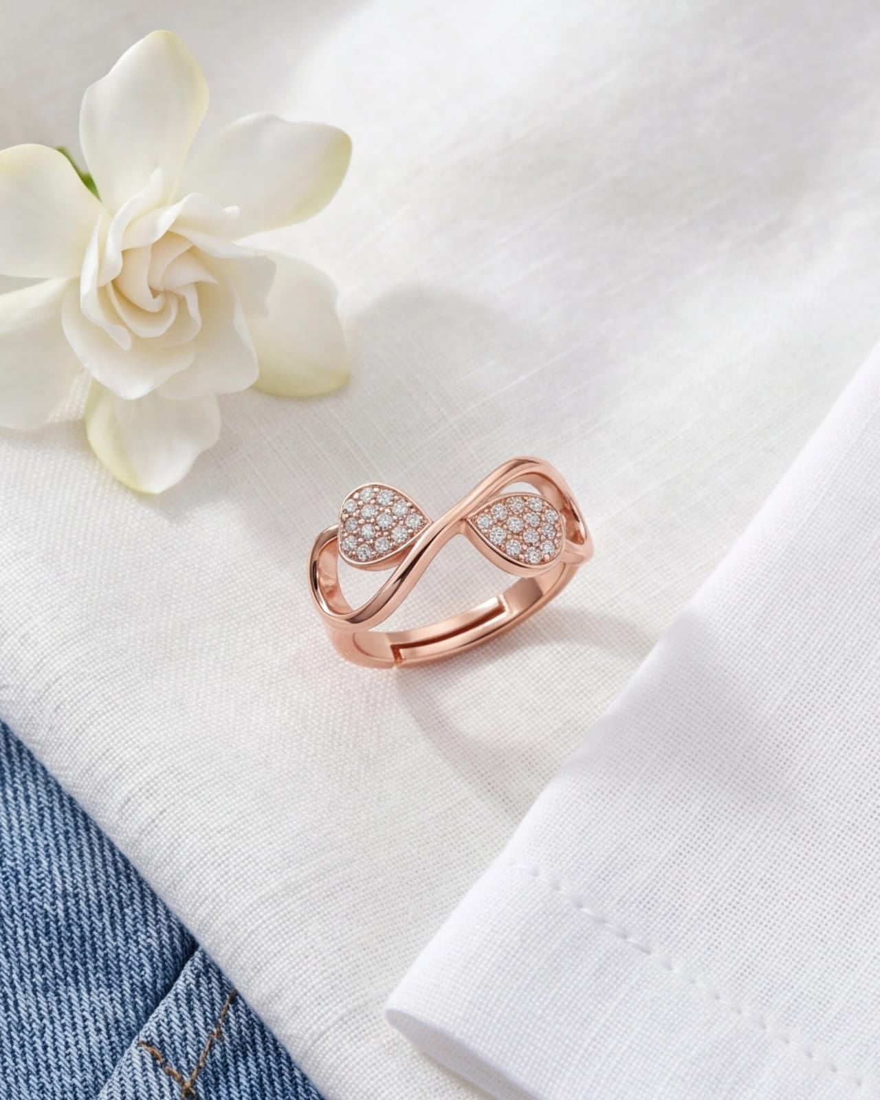 Rose gold ring with heart-shaped gemstones on a white fabric background with a white flower. #color_rose gold