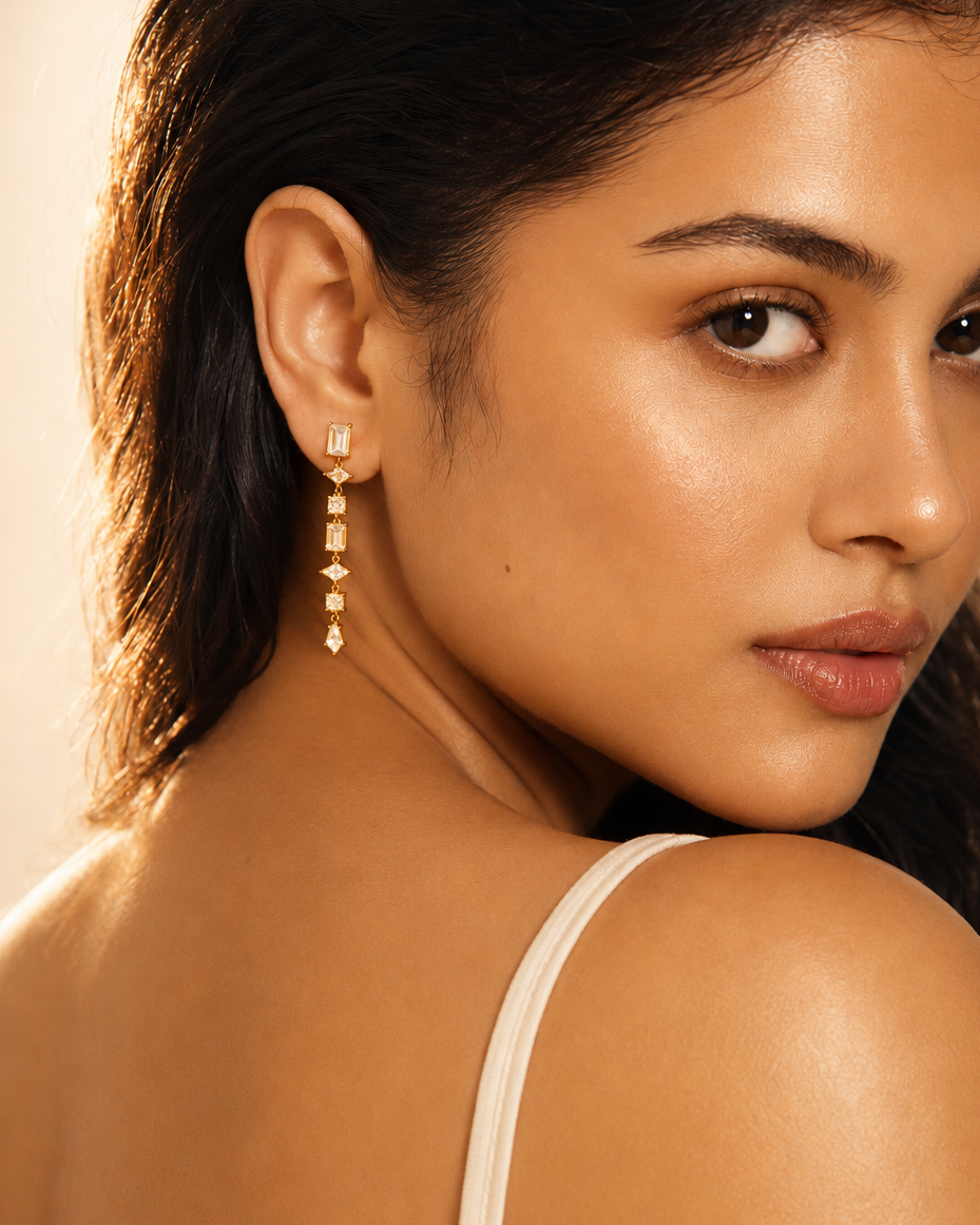 Close-up of a woman wearing a dangling earring with a neutral background #color_rose gold
